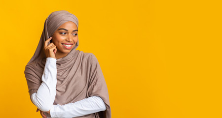 Interested black muslim girl looking away at copy space on yellow background