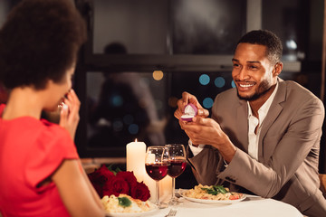 Afro man proposing to girlfriend holding ring dating in restaurant