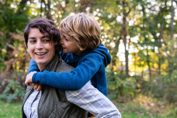 mother giving her daughter a piggyback ride in a park