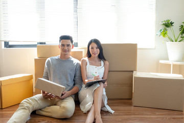 Happy young Asian couple sitting together and smiling during moving to new house