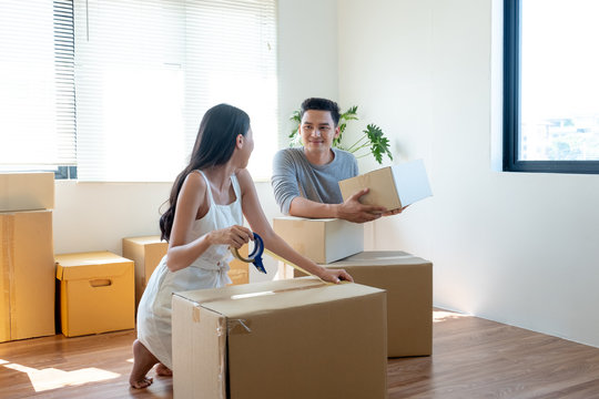 Young Asian couple helping each other to packing and holding box for moving new house