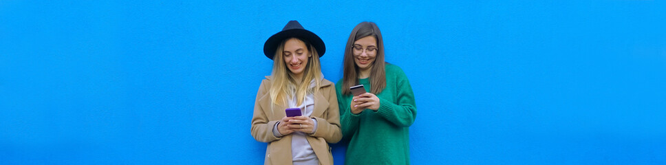 Girls in a blu background taking selfie - Teenagers posing cheerfully with mobile phone in hand - Technology as a lifestyle concept