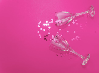 Flat lay celebration. Holiday concept for Valentine's Day, Christmas, New Year, birthday. Glasses for wine or champagne lie on a pink background and decorated with pink confetti hearts.