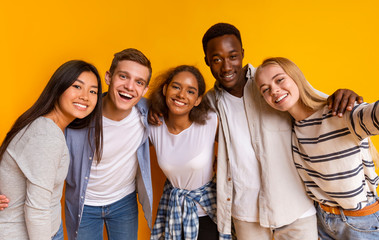 Friendly international students taking selfie over yellow background