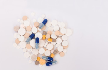 Heap of colorful pills in the shape of a heart, tablets and capsules on white background. Drug prescription for treatment medication health care concept, top view with copy space.