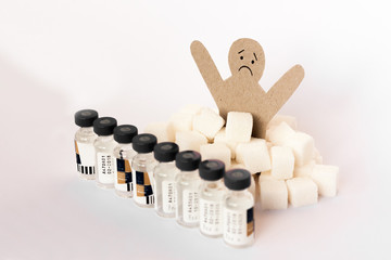 figure of a cardboard man surrounded by refined sugar cubes and bottles of insulin on white background, diabetes protection medical concept.