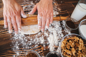 Woman is rolling pin on dough in kitchen, dough recipe ingredients and rolling pin on vintage wood table from above.