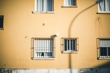 Fototapeta na wymiar Fachada amarilla con ventanas con rejas y sombras de farola