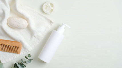 Obraz na płótnie Canvas Beauty SPA cosmetic bottle container, towel, wooden hair comb, organic soap, luffa sponge, eucalyptus leaf on green background. Minimalist cosmetic product mockup, natural branding
