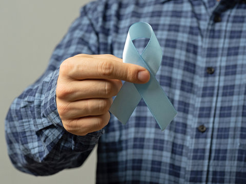 A man in a blue plaid shirt holds a blue ribbon. A sign of the fight against prostate cancer. ?oncept of medicine and means of health care.