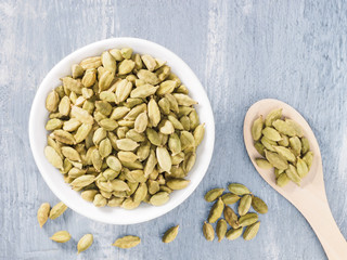 Spice green cardamom (Elettaria cardamomum) in a ceramic white bowl and wooden spoon on gray concrete background. The proper nutrition concept