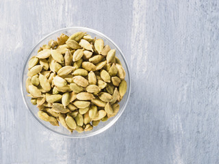 Spice green cardamom (Elettaria cardamomum) in transparent bowl on gray concrete background closeup. The proper nutrition concept