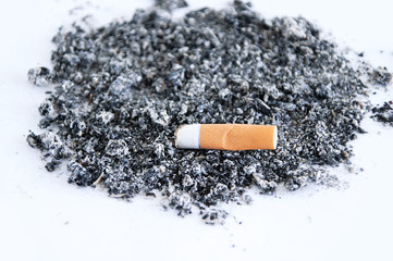 Cigarette butt with a yellow filter on a pile of ash on a white background.