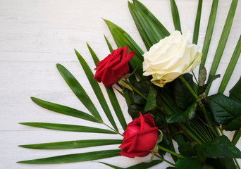 A bouquet of three fresh red and white roses with decorative green palm leaves on the light grey, top view flat lay floral composition