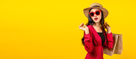 Banner of Asian trendy shopaholic woman excited about new purchases or sales holding shopping bags and looking to side copy space over yellow background. Happy Asian customer carrying shopping bags.