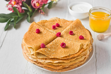 Stack of russian pancakes (crepes) with raspberry, honey and sour cream