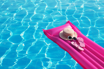 Beach summer holiday background. Inflatable air mattress, flip flops and hat on swimming pool.