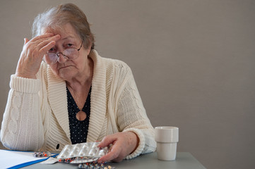 Elderly woman with beautiful wrinkled face is holding pills in her hands to choose medicines. Selective focus depth of field