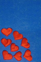 Vertical top view of red hearts in corner on blue cardboard background. Valentines Day concept, copy space.