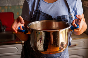 woman cook in an apron prepares tomatoes in a saucepan, rubs through a sieve and prepares tomato juice. Female hands closeup.