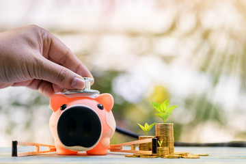 Man hand hold is use a stethoscope with check hygiene of the sick piggy bank use underarm crutches and stacked gold coin on sunlight in the public park, saving money for buy health insurance concept.