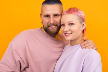 valentine's day concept. portrait of a happy couple of husband and wife with colored hair and piercings dressed in pink clothes stand in an embrace on a yellow background