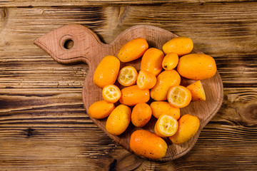 Cutting board with kumquat fruits on wooden table. Top view