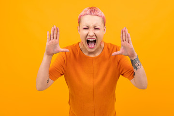 Extraordinary beautiful woman with short pink hair and big tattoo on her hand screams isolated on orange background