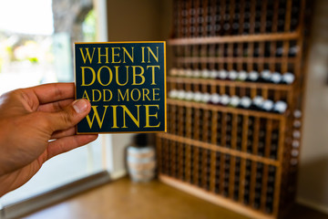 When in doubt add more wine, hand holding quote sign selective focus view against wine tasting room...
