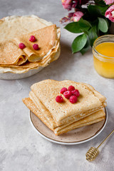 Stack of russian pancakes (crepes) with raspberry, honey and flowers. Traditional Maslenitsa (Shrovetide) meal.