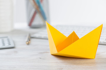 Workspace with office desk and yellow paper ship