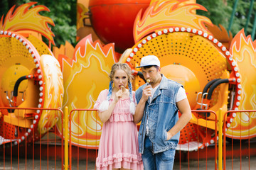 Obraz na płótnie Canvas Bright cheerful couple in love resting in an amusement Park. Funny guy and girl eating lollipops on a stick