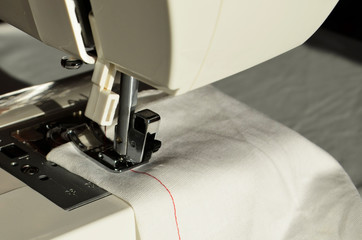 The sewing machine is filled with red thread for sewing and white fabric for work.