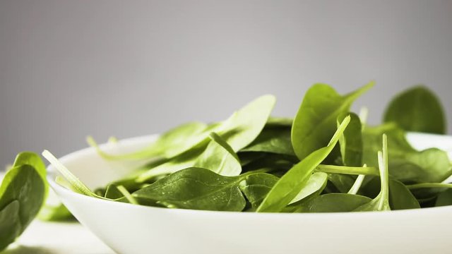 Fresh spinach leaves fall in a bowl, slow motion.