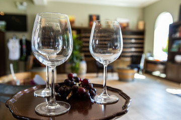 three wine empty glasses on small table with black red grapes selective focus, winery cellar tasting room bottles racks shelves display background