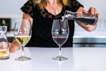 female bartender hand close up as she pouring red wine from a small mini decanter to the wineglass, next to a white glass of wine, bright bar counter