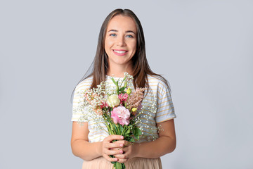 Portrait of happy woman with bouquet on grey background