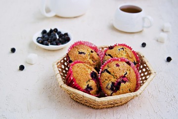 Muffins with black currants in a wicker basket on a light concrete background. American cuisine. Copyspace. Selective focus