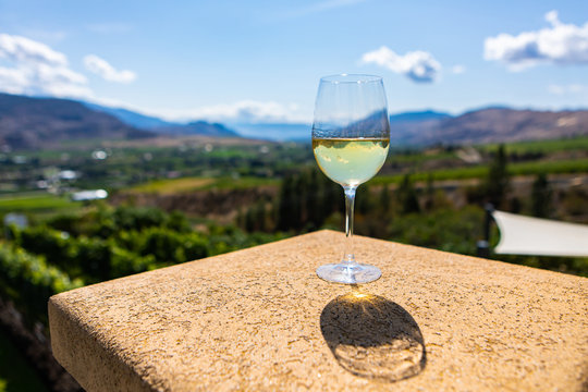 A Canadian glass of white wine on building top selective focus view against vineyard background, Okanagan Valley, British Columbia, Canada