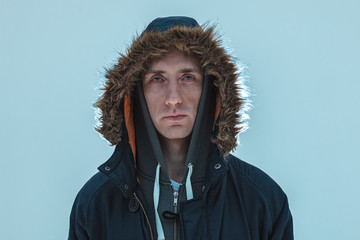 serious middle age caucasian man in winter parka with hood isolated on blue background © Sergey Chumakov