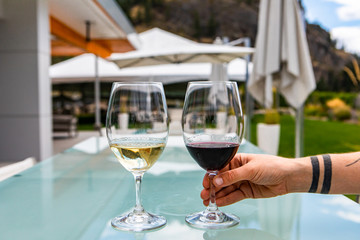 hand holding choosing red wine glass from Two Glasses of Red and white wines on the outdoor restaurant dining table, patio umbrellas in the background