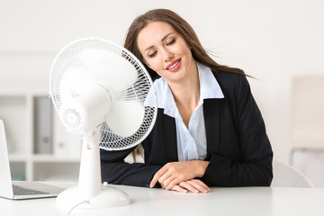Young woman using electric fan during heatwave in office