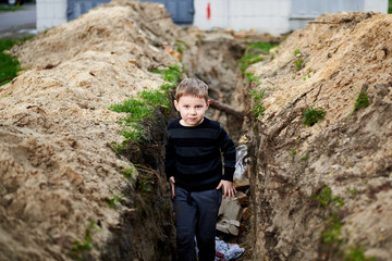 A trench dug in the ground in which a little boy plays.