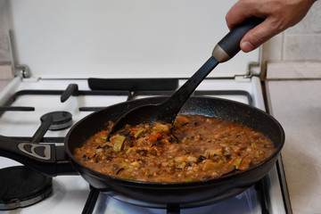 man cooks sauteed vegetables in a pan in the kitchen