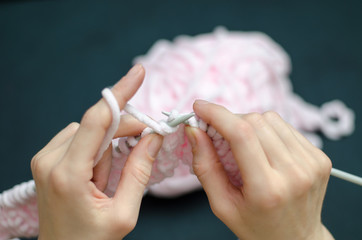A young girl knits something with pink threads, black background