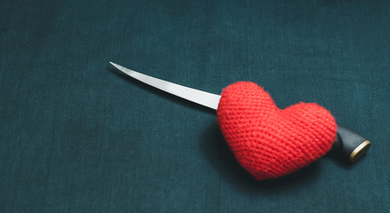 Red heart and knife on a black background. Mystical photo