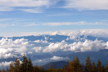 High, blue mountains partly covered in clouds. Some blue sky and a forest in the foreground