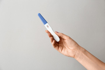 Female hand with pregnancy test on grey background