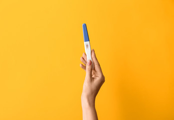 Female hand with pregnancy test on color background