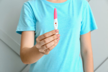 Young woman with pregnancy test on grey background